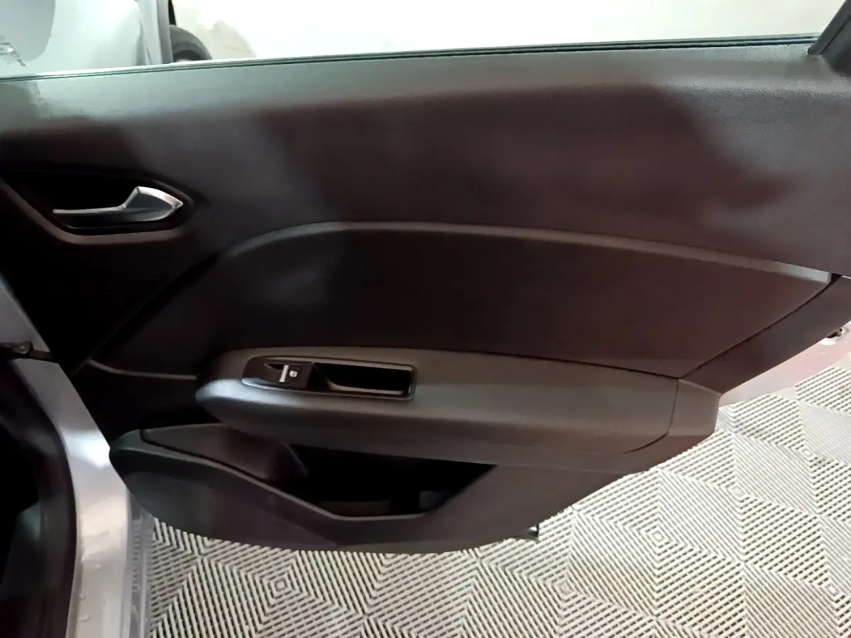 Vue intérieure du panneau de porte côté gauche du Renault Captur gris clair, avec poignée et commande de vitre électrique.