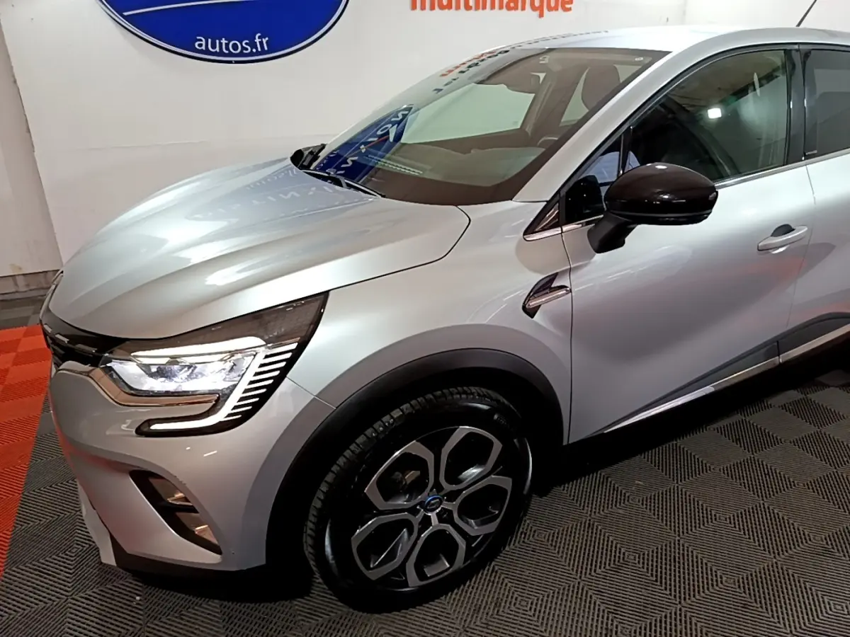 Vue 3/4 avant droit d’un Renault Captur Intens E-Tech hybride rechargeable gris clair avec phares LED et jantes distinctives.