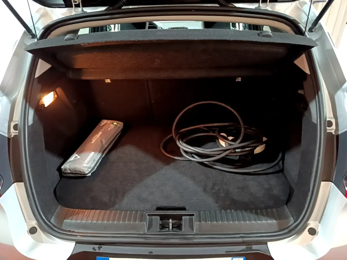 Coffre ouvert vu de l'arrière d'un Renault Captur gris clair avec câble de recharge et trousse de secours visible.