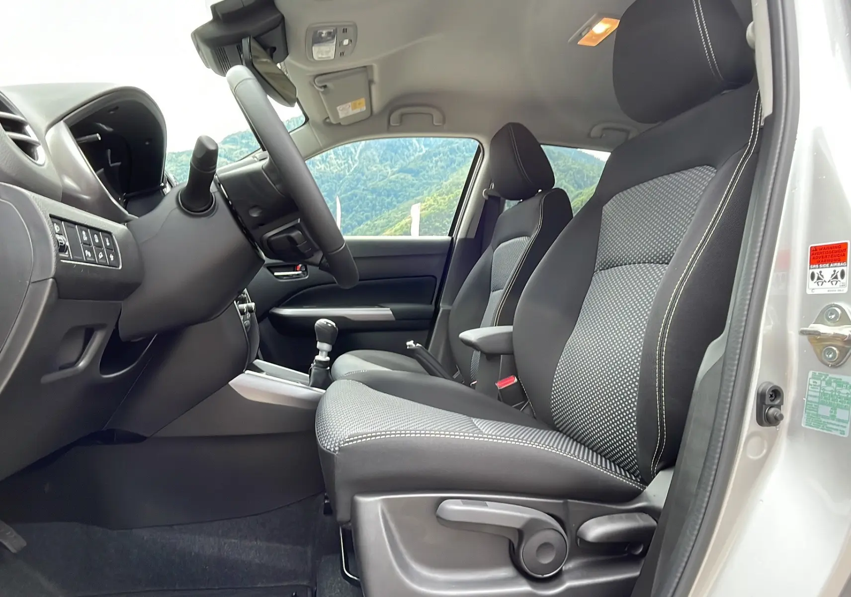 Vue intérieure côté conducteur du Suzuki Vitara 2025 gris argent avec sièges tissu noir et console centrale manuelle.