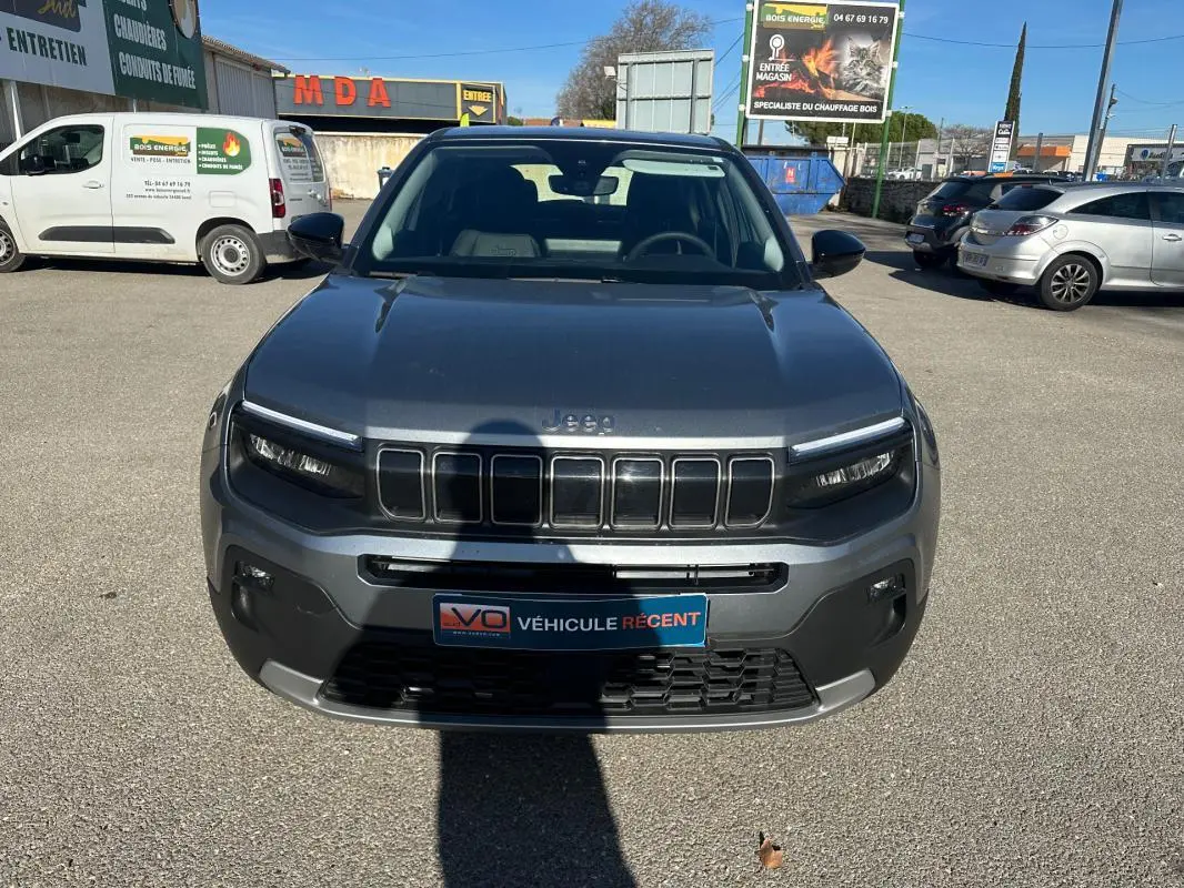 Vue de face d'une Jeep Avenger gris métallisé 2025 avec calandre distinctive et phares LED allumés.