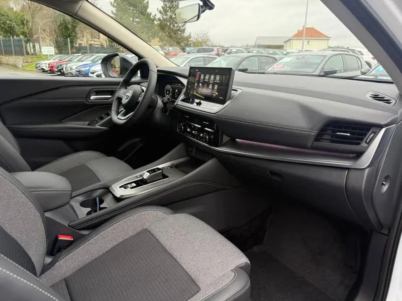 Vue intérieure côté conducteur du Nissan Qashqai Hybrid e-POWER 2025, avec tableau de bord moderne et écran tactile central.