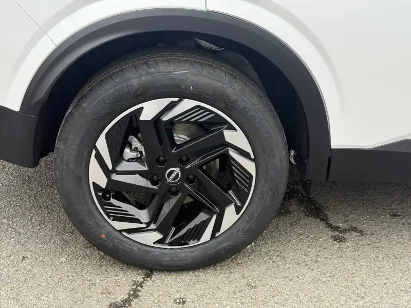 Gros plan sur la roue avant gauche du Nissan Qashqai Hybrid e-POWER 2025 en blanc nacré avec jante noire et argentée au design anguleux.