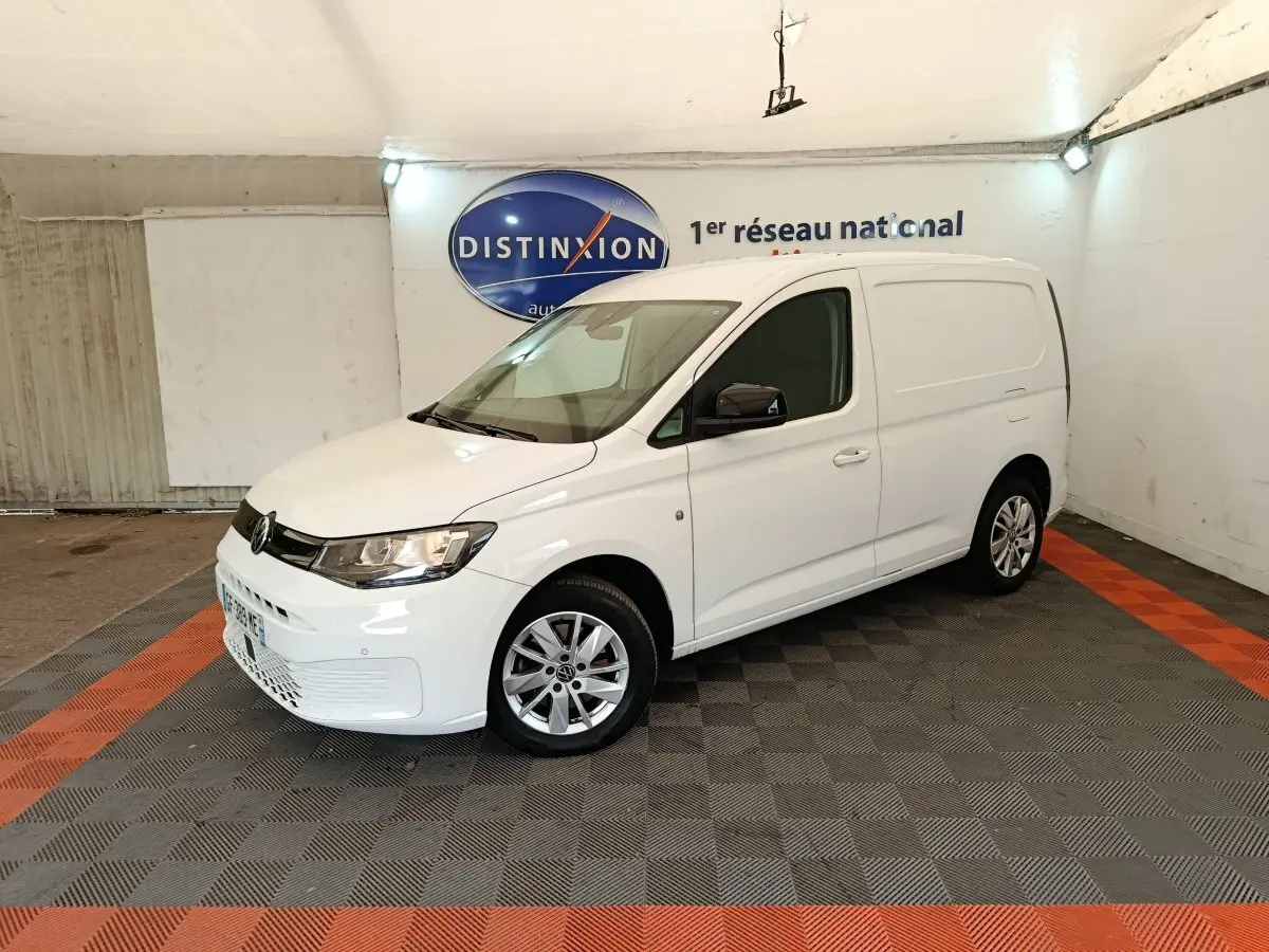 Vue 3/4 avant droit d'un Volkswagen Caddy blanc 2022 avec jantes alliage et rétroviseurs noirs dans un garage.