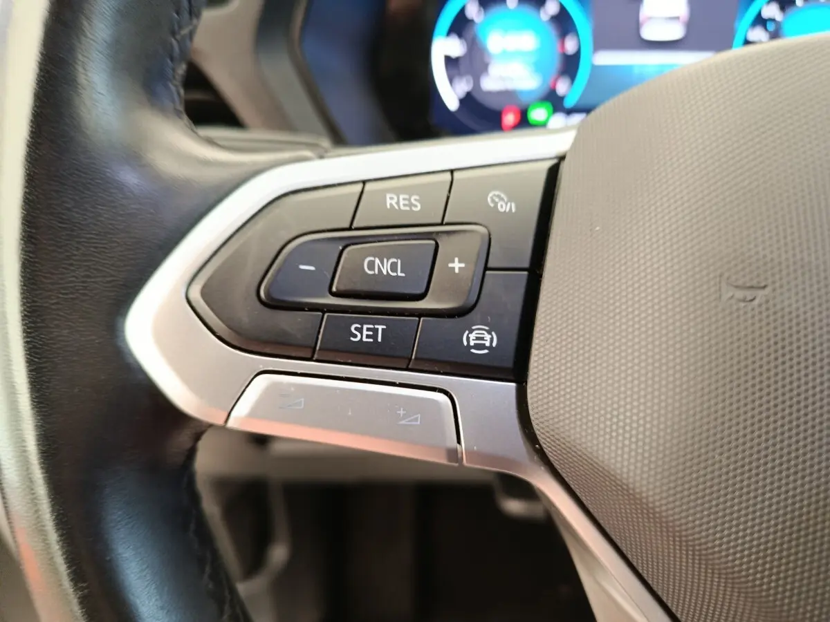 Gros plan sur les commandes du volant cuir noir du Volkswagen Caddy blanc, avec boutons multifonctions et régulateur de vitesse.