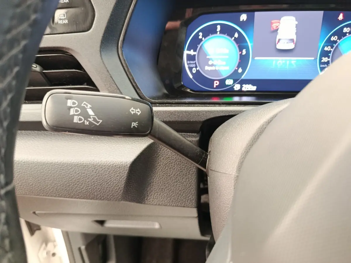 Gros plan sur le commodo gauche du volant d’un Volkswagen Caddy 2.0 TDI blanc, avec tableau de bord numérique en arrière-plan.