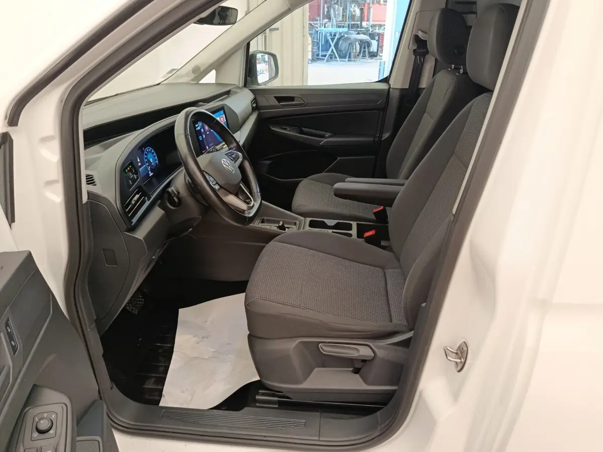 Vue intérieure côté conducteur du Volkswagen Caddy blanc 2022, avec tableau de bord numérique et volant cuir multifonctions.