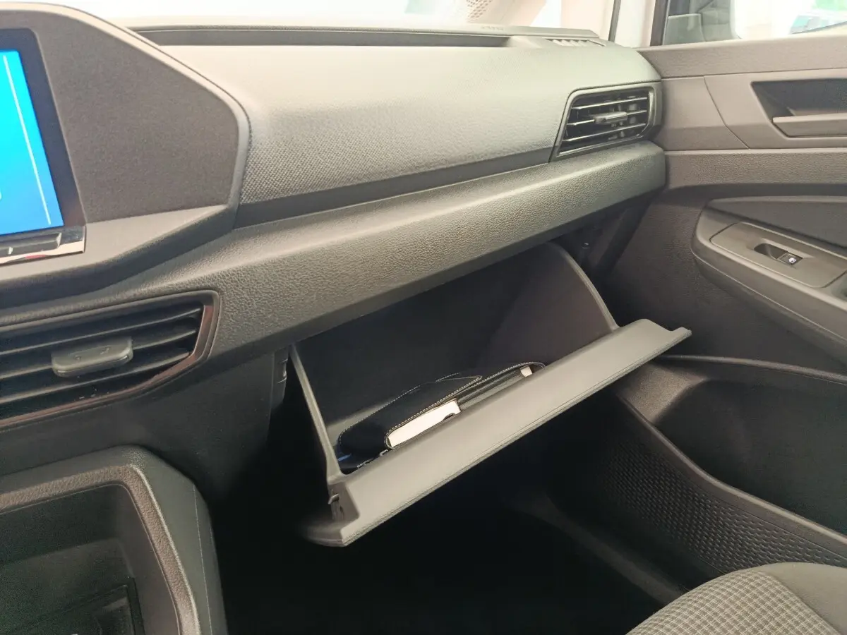 Intérieur du Volkswagen Caddy 2022, vue côté passager sur la boîte à gants ouverte et tableau de bord noir.