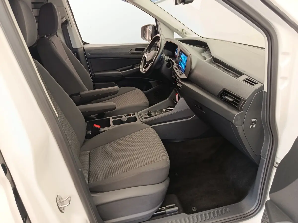 Vue intérieure côté passager du Volkswagen Caddy blanc 2022, mettant en valeur les sièges gris et l'écran tactile central.