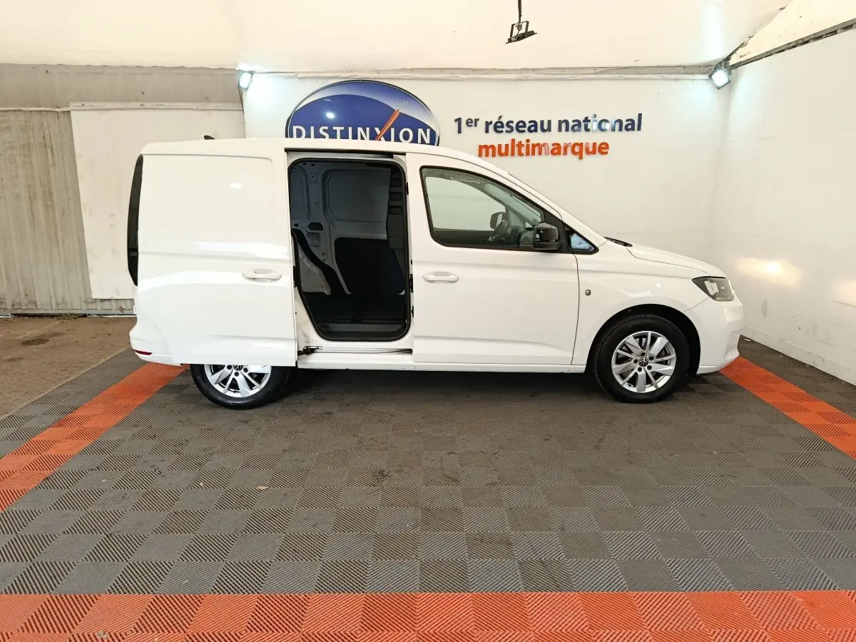 Vue de profil côté droit du Volkswagen Caddy blanc 2022 avec porte coulissante arrière ouverte en intérieur showroom.