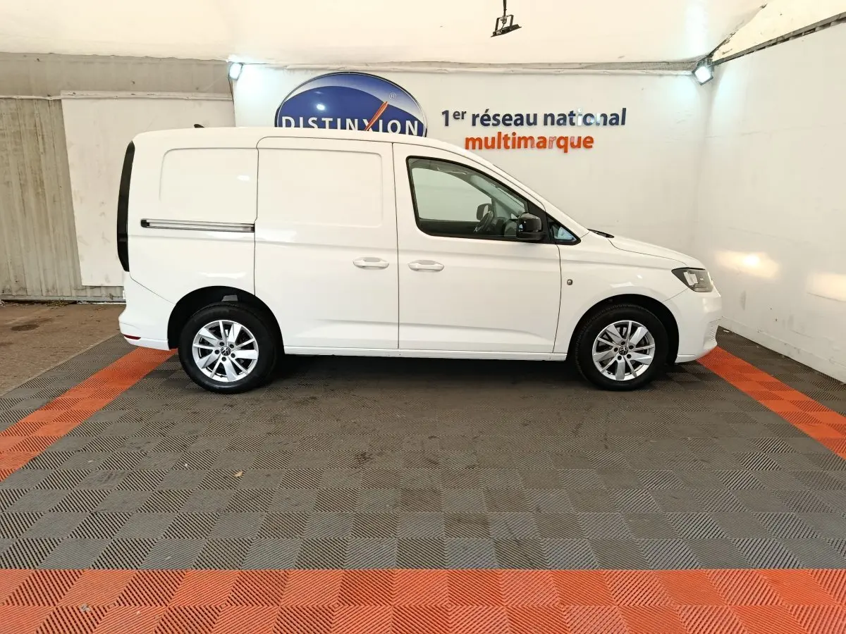 Vue de profil côté droit d'un Volkswagen Caddy blanc 2022 en intérieur sur sol gris et orange.