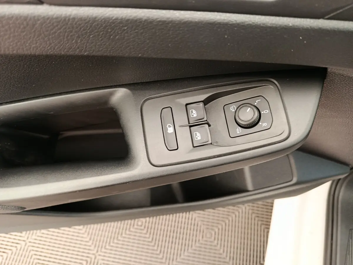 Détail des commandes de réglage des rétroviseurs et des vitres sur la porte côté conducteur d’un Volkswagen Caddy blanc.