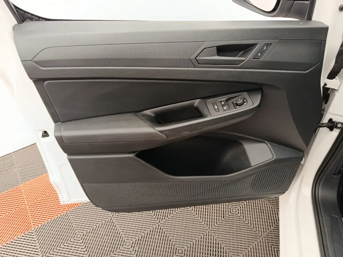 Vue rapprochée de la porte avant gauche blanche du Volkswagen Caddy 2022 avec commandes électriques et poignée noire.