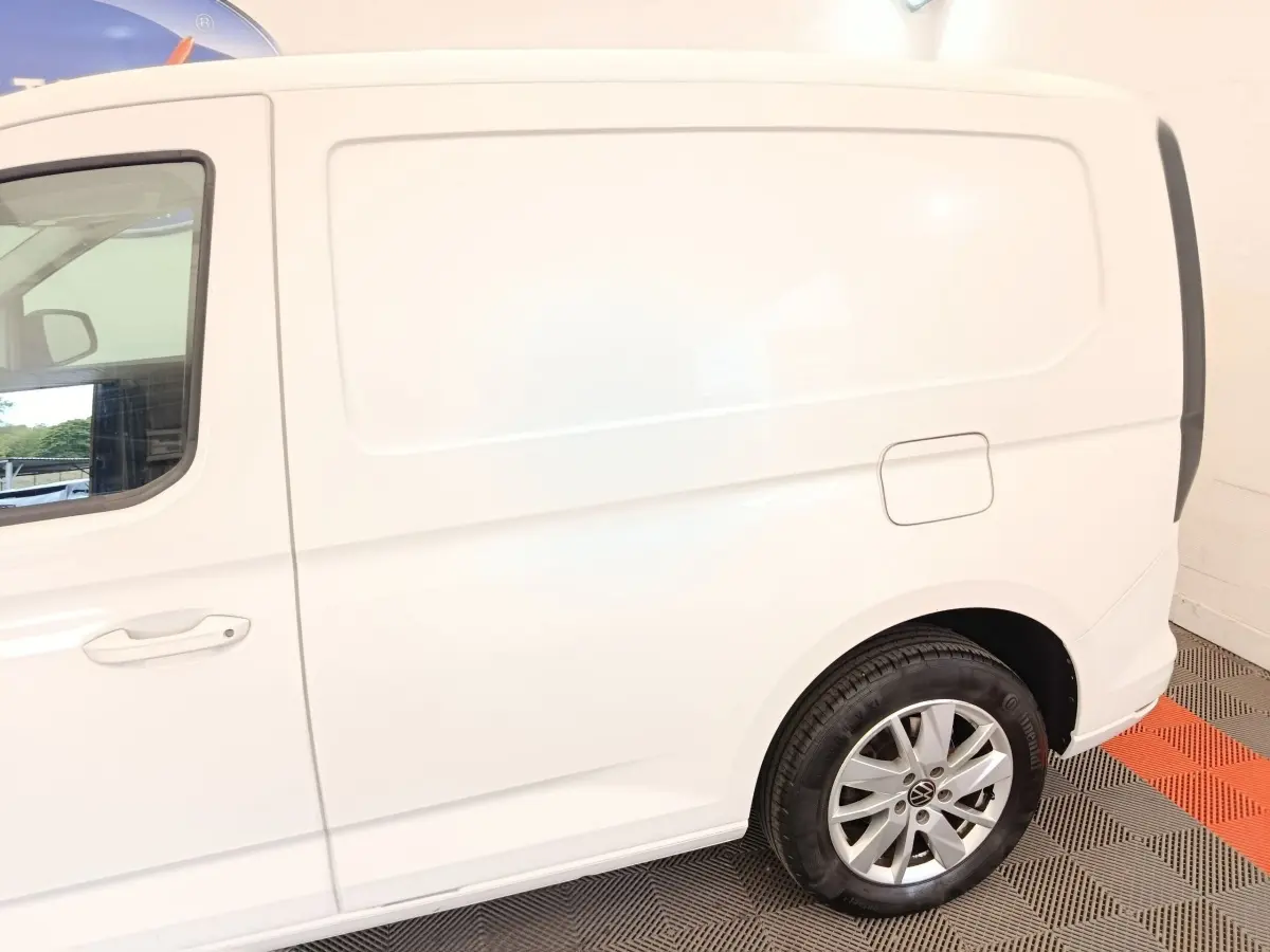Vue latérale droite du Volkswagen Caddy blanc, mettant en valeur la porte latérale et la roue arrière avec jante alliage.