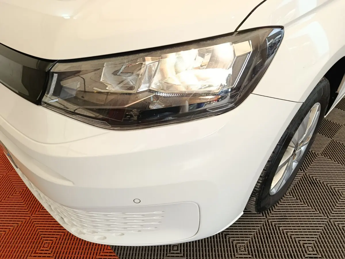 Gros plan sur l'avant droit blanc d'un Volkswagen Caddy 2022, mettant en valeur le phare et la roue.