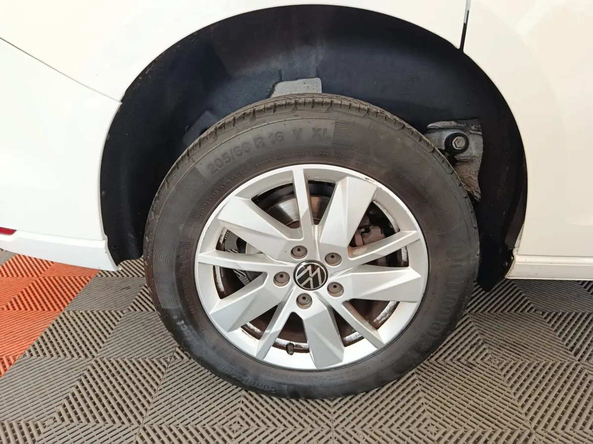 Gros plan sur la roue avant gauche du Volkswagen Caddy blanc, avec jante alliage argentée et logo VW central.