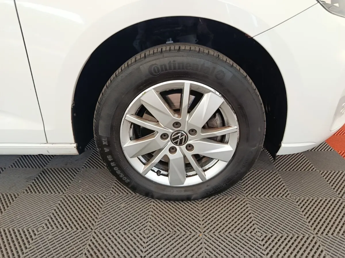 Gros plan sur la roue avant gauche d'un Volkswagen Caddy blanc, mettant en valeur la jante alliage et le pneu Continental.