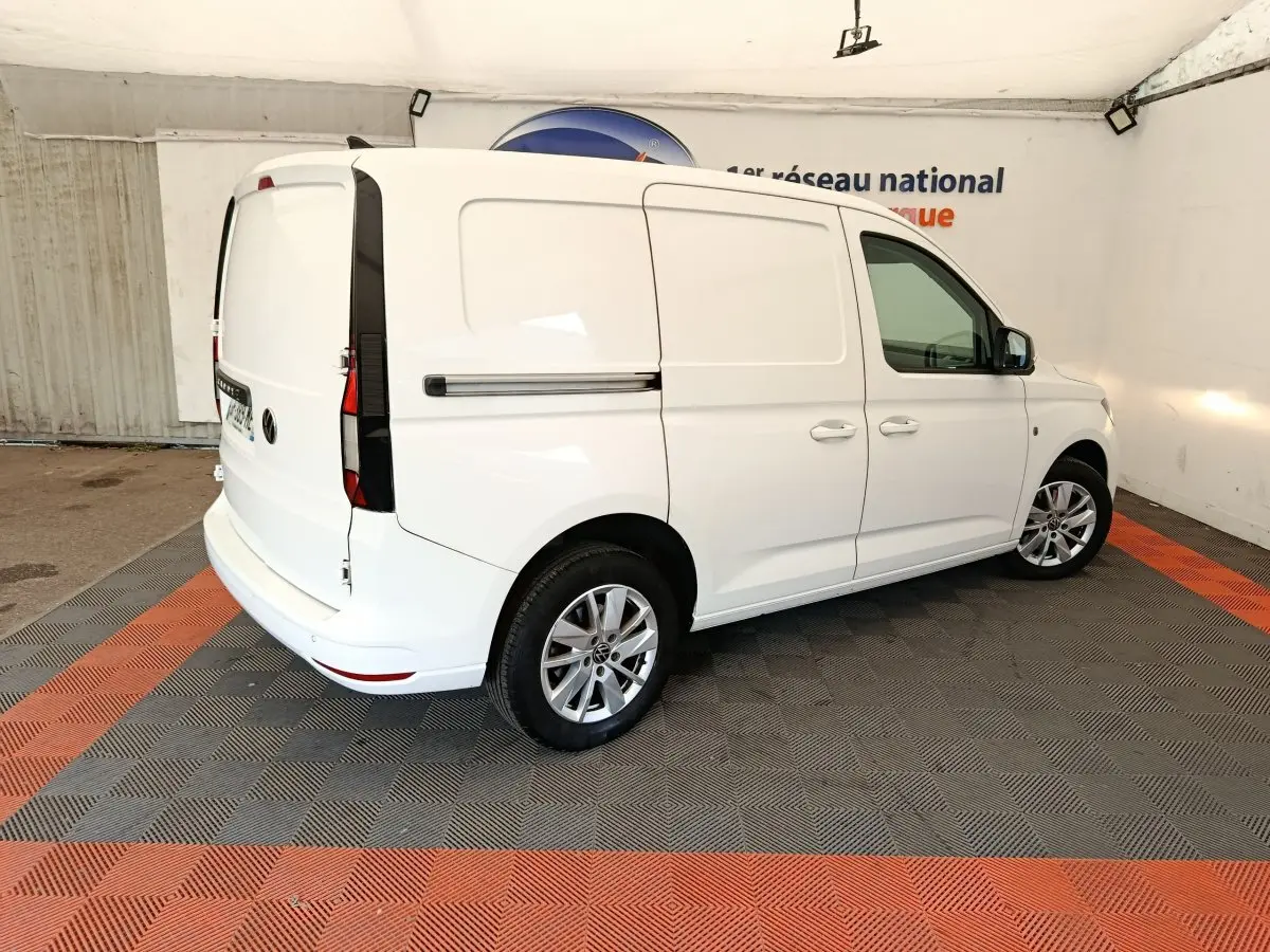 Vue 3/4 arrière droite d'un Volkswagen Caddy blanc, fourgon utilitaire avec jantes alliage et portes latérales pleines.
