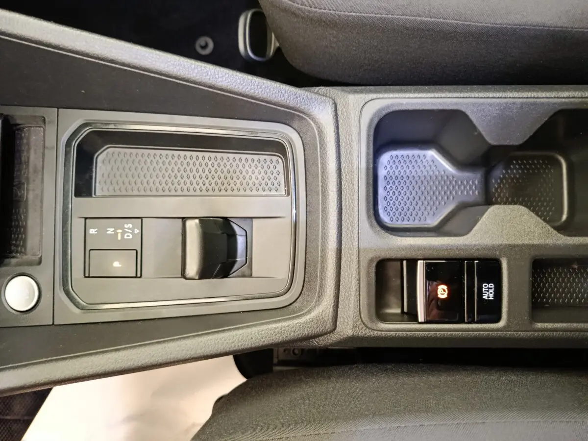 Vue rapprochée de la console centrale noire du Volkswagen Caddy 2022, avec levier de boîte auto et frein à main électrique.