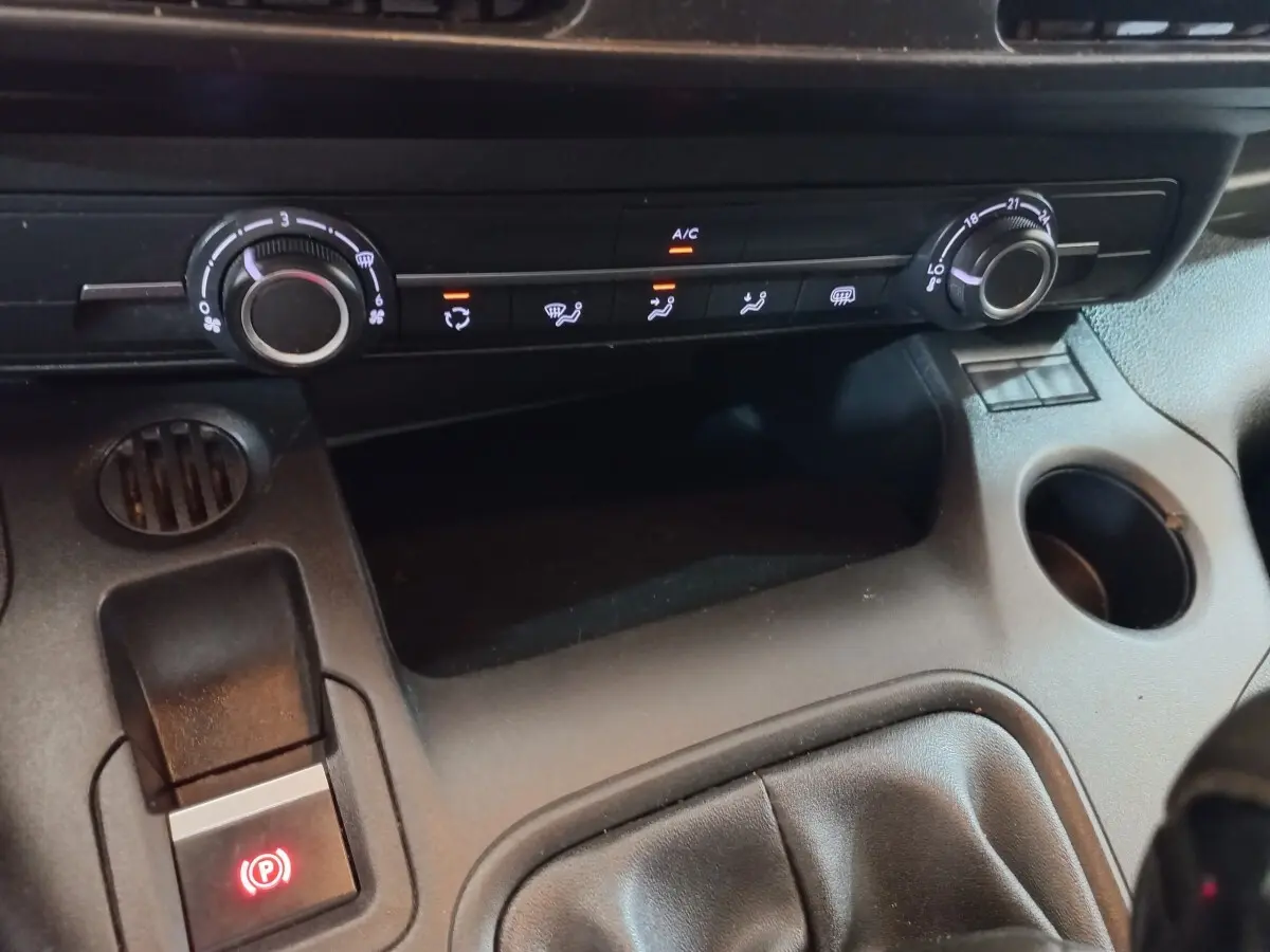 Détail intérieur du tableau de bord du Peugeot Partner blanc 2021, avec commandes de climatisation et frein à main électrique.