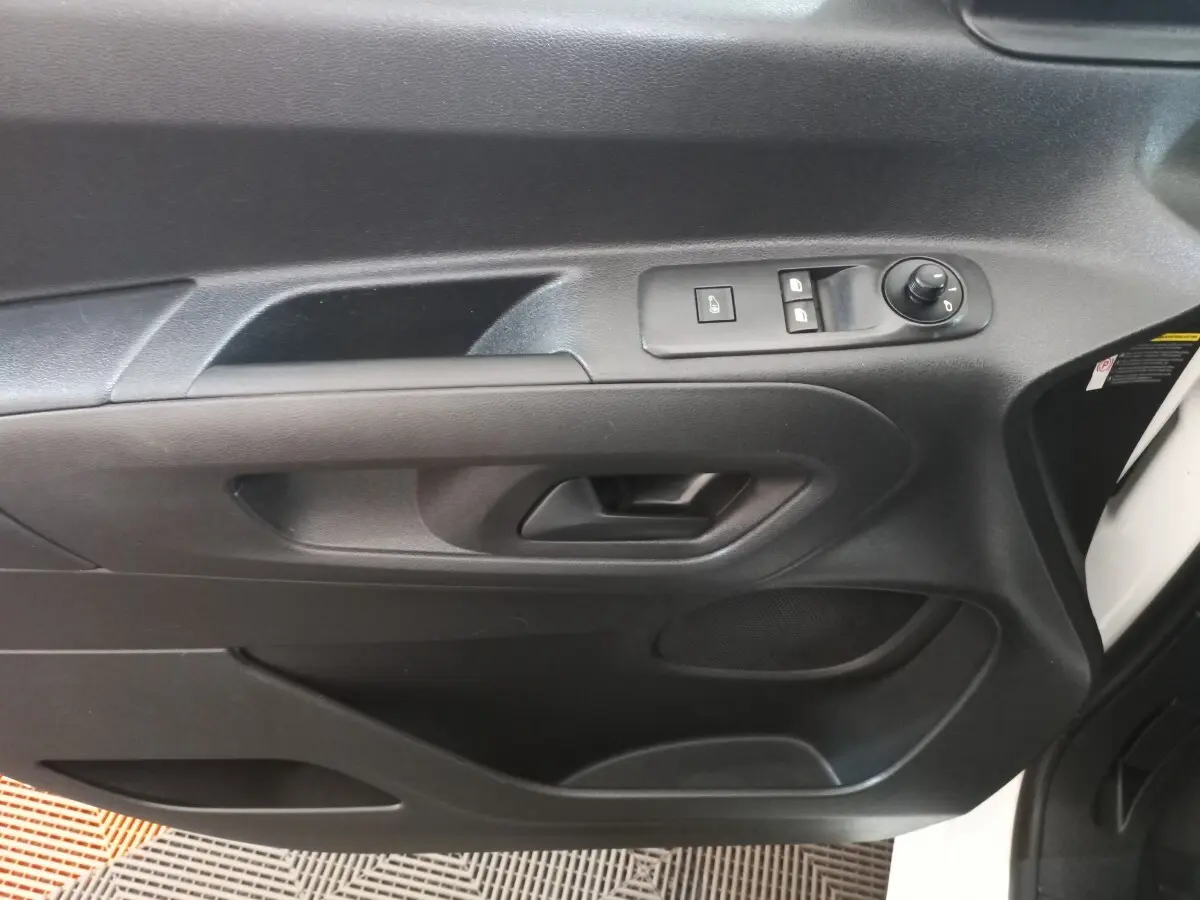 Vue rapprochée de la porte intérieure côté conducteur du Peugeot Partner blanc, avec commandes de vitres et rétroviseur.
