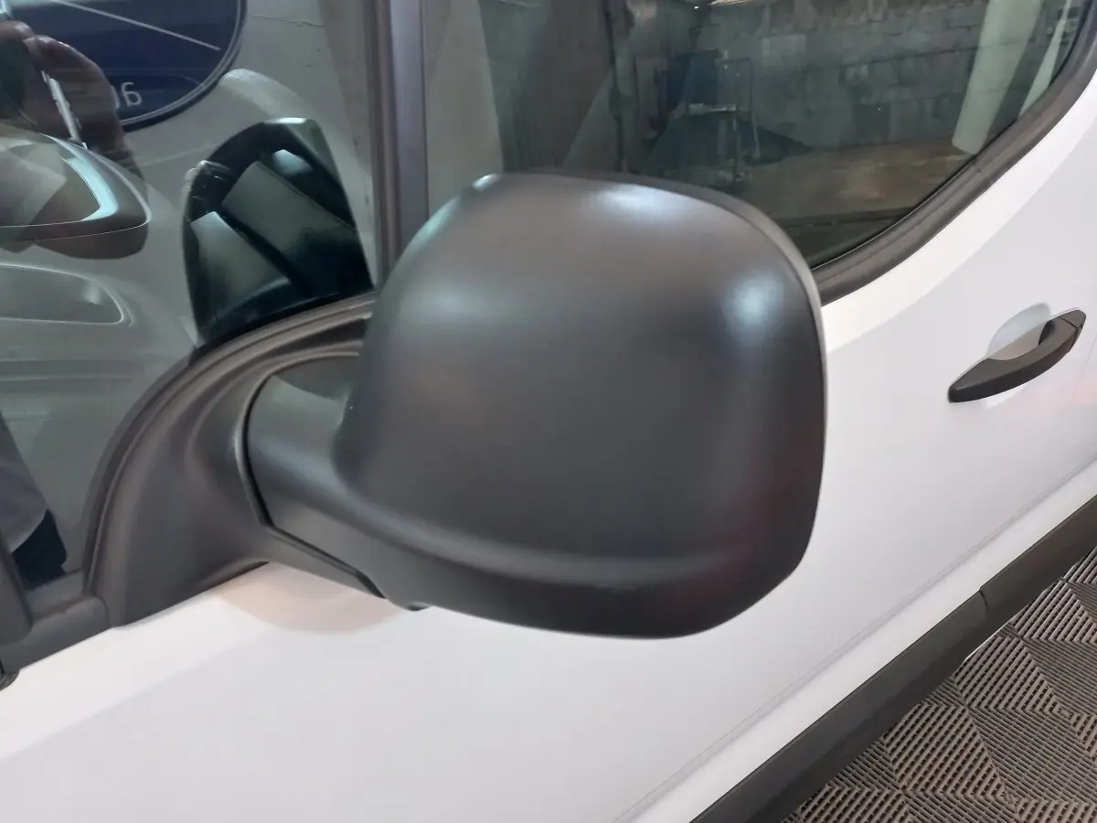 Gros plan sur le rétroviseur côté conducteur noir d’un Peugeot Partner blanc, vue latérale avant droite.