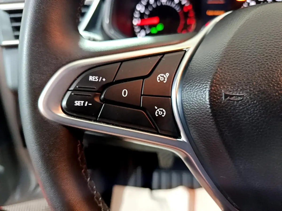 Gros plan sur les commandes du régulateur de vitesse à gauche du volant cuir noir de la Renault Clio gris clair 2023.