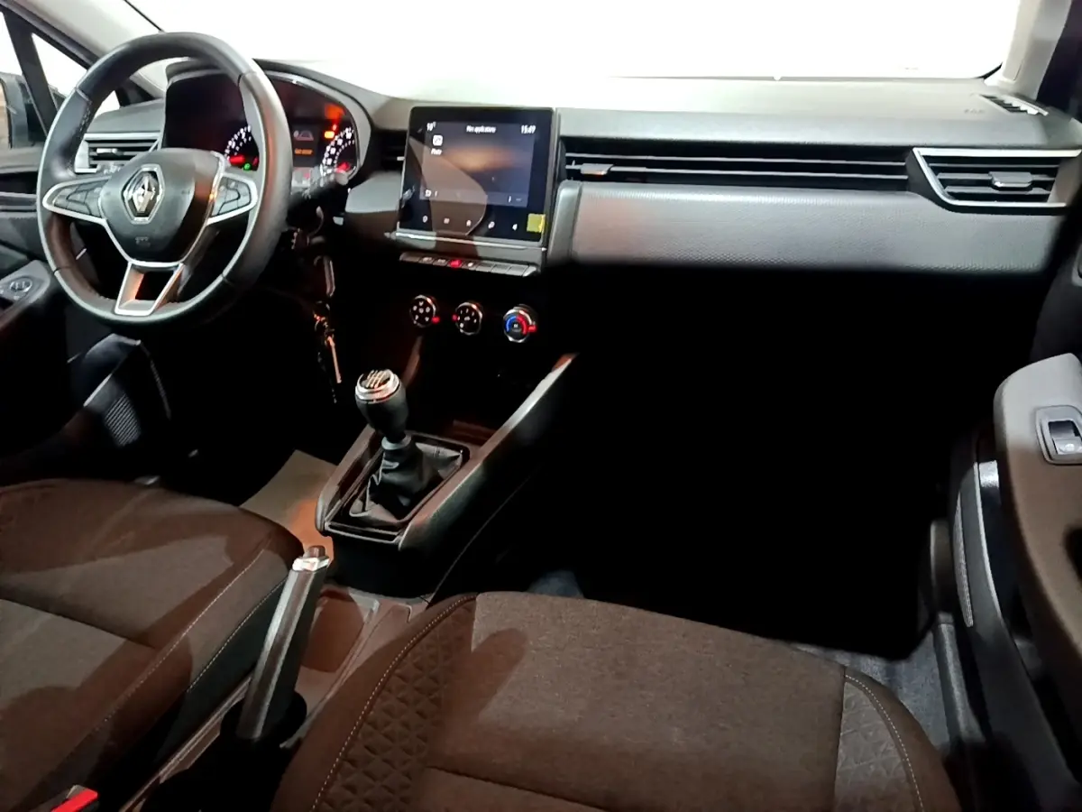 Vue intérieure côté conducteur de la Renault Clio gris clair 2023, volant cuir, écran tactile central et boîte manuelle.