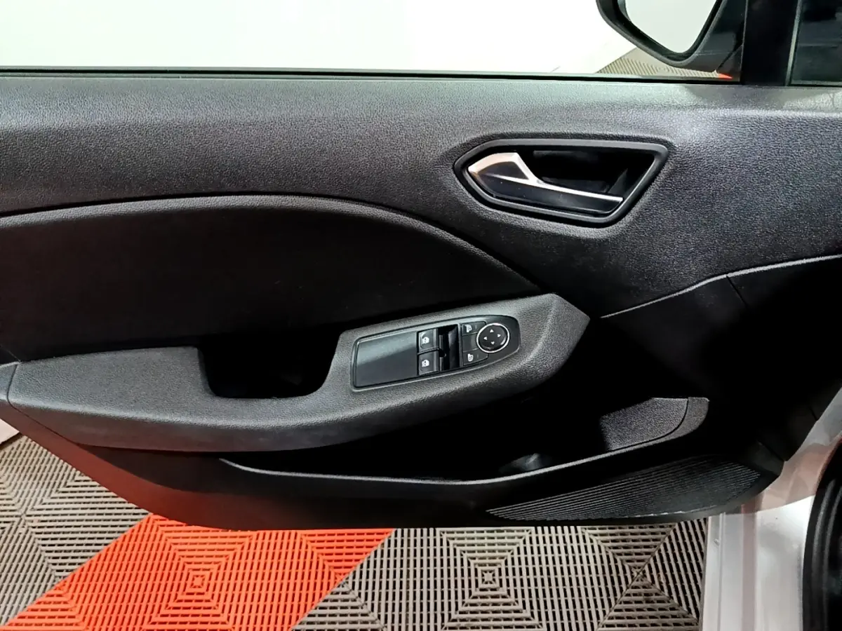 Vue rapprochée de la porte avant gauche de la Renault Clio gris clair, avec commandes électriques des vitres et poignée intérieure noire.