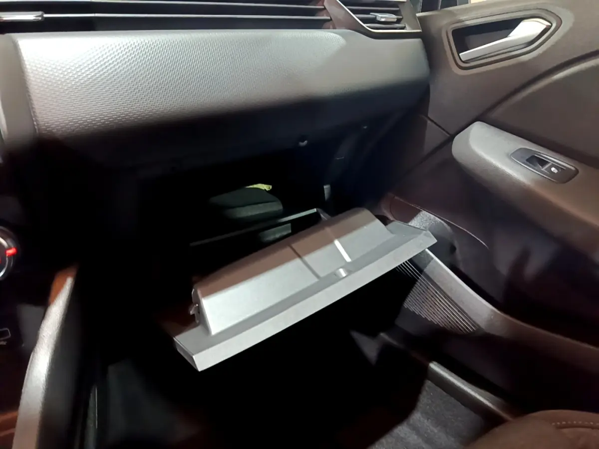 Intérieur Renault Clio 2023 gris clair, vue côté passager sur boîte à gants ouverte et tableau de bord texturé.