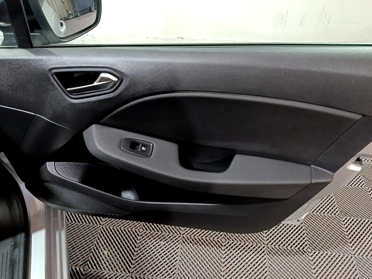 Vue intérieure du panneau de porte côté gauche gris foncé de la Renault Clio 2023, avec poignée et commande de vitre électrique.