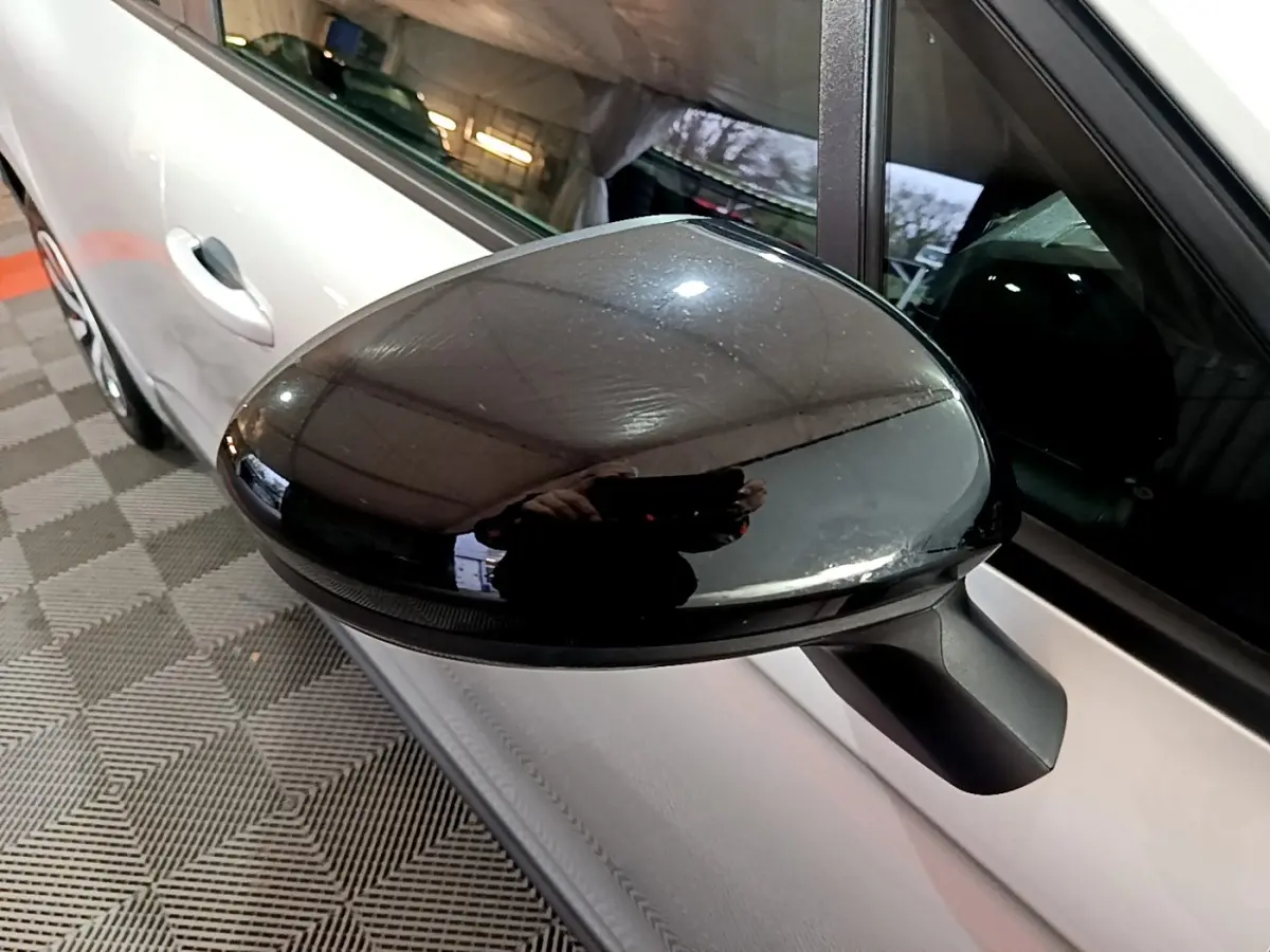 Gros plan sur le rétroviseur noir côté gauche d'une Renault Clio gris clair, vue partielle de la portière avant.