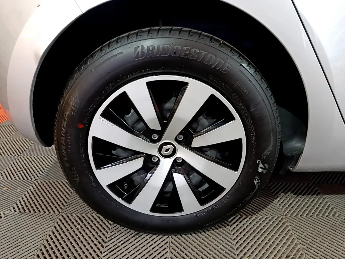 Gros plan sur la roue avant droite d'une Renault Clio gris clair 2023 avec jante alliage bicolore et logo Renault central.