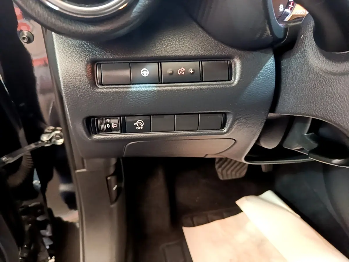 Vue intérieure côté conducteur du tableau de bord noir avec commandes d’éclairage et réglage du volant d’un Nissan Juke 2022.