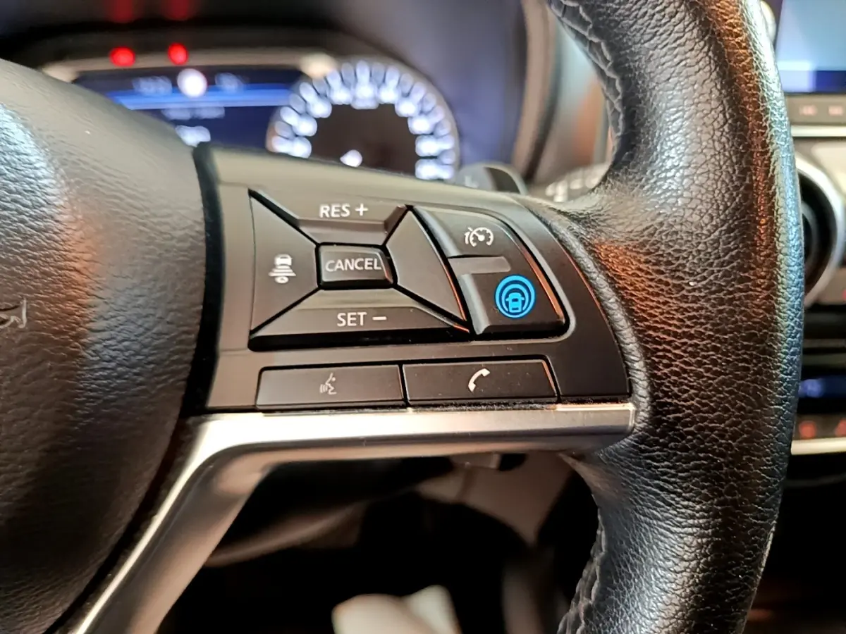 Gros plan sur les commandes du volant noir du Nissan Juke 2022, avec affichage digital flou en arrière-plan.