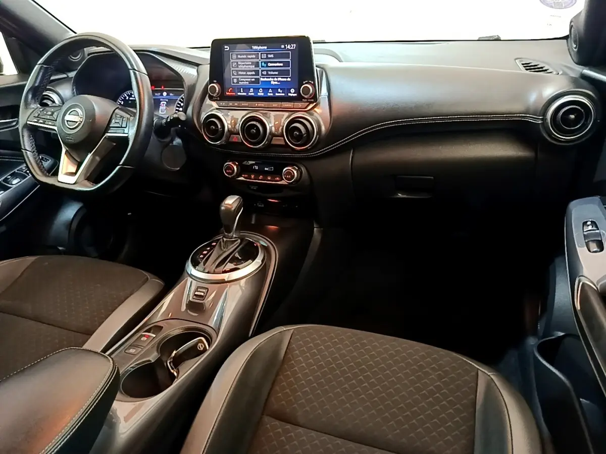Vue intérieure avant du Nissan Juke 2022 noir, tableau de bord avec écran tactile central et volant multifonctions.