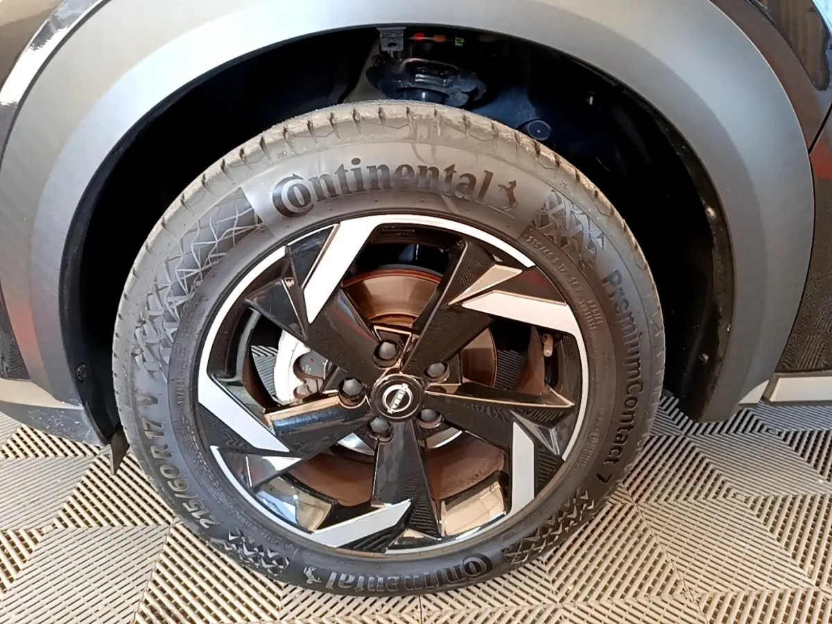 Gros plan sur la roue avant droite du Nissan Juke noir 2022 avec jante alliage bicolore et pneu Continental.