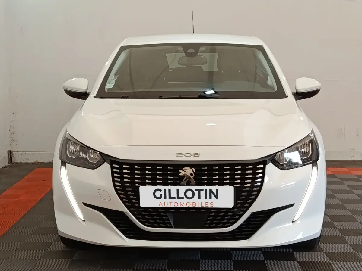 Peugeot 208 blanc vue de face avec calandre noire et feux LED en forme de griffes allumés.