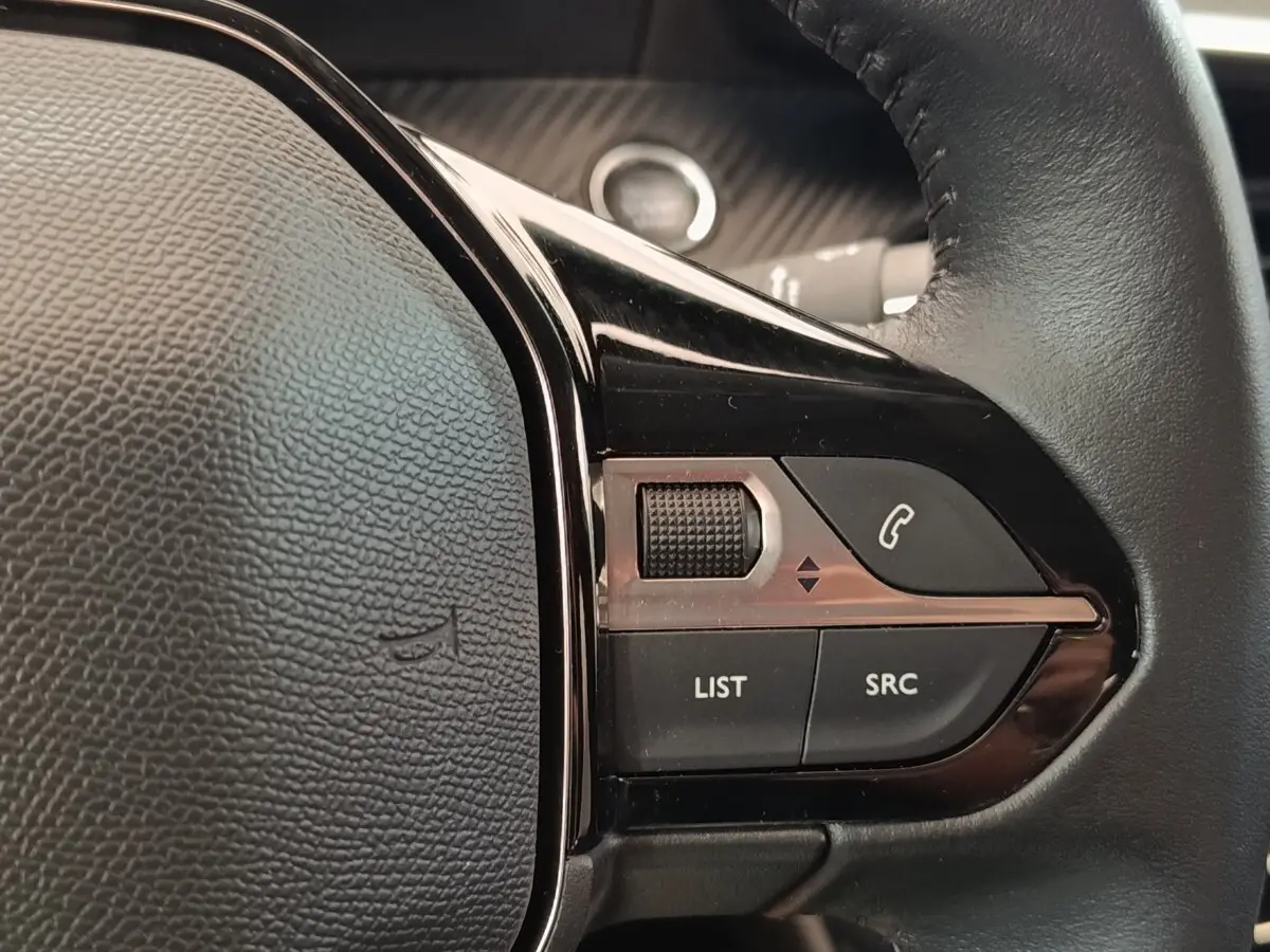 Gros plan sur les commandes gauche du volant cuir noir du Peugeot 208 blanc, avec bouton appel et molette de réglage.