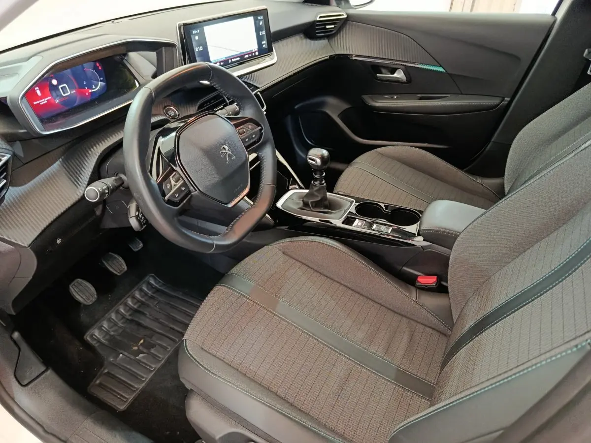 Vue intérieure côté conducteur de la Peugeot 208 2021, volant cuir, écran tactile 10 pouces et sièges gris.