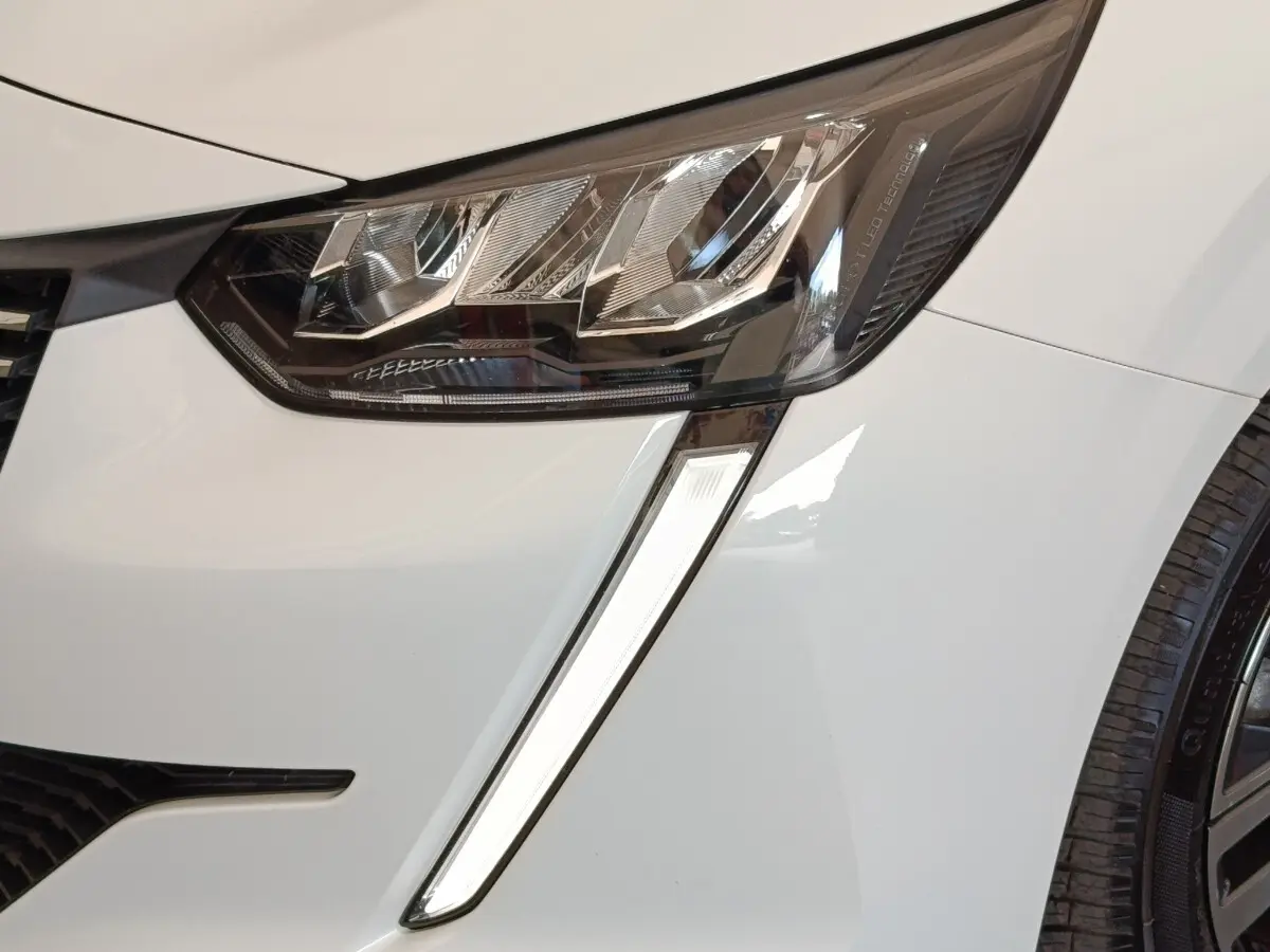 Gros plan sur le phare avant droit LED et la carrosserie blanche d'une Peugeot 208 PureTech 100 S&S Allure Business.