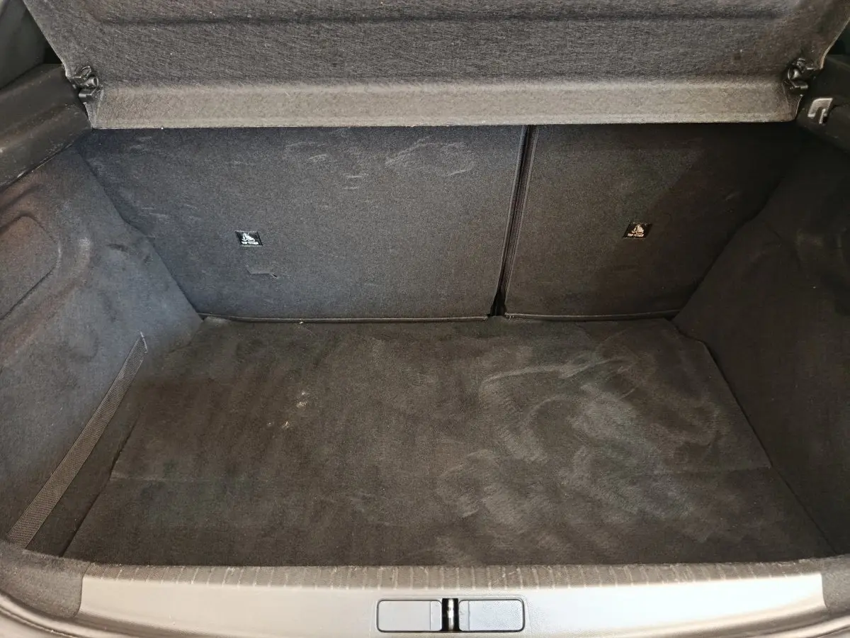 Coffre ouvert vu de face, intérieur noir, sans chargement, de la Peugeot 208 PureTech 100 S&S Allure Business blanche.