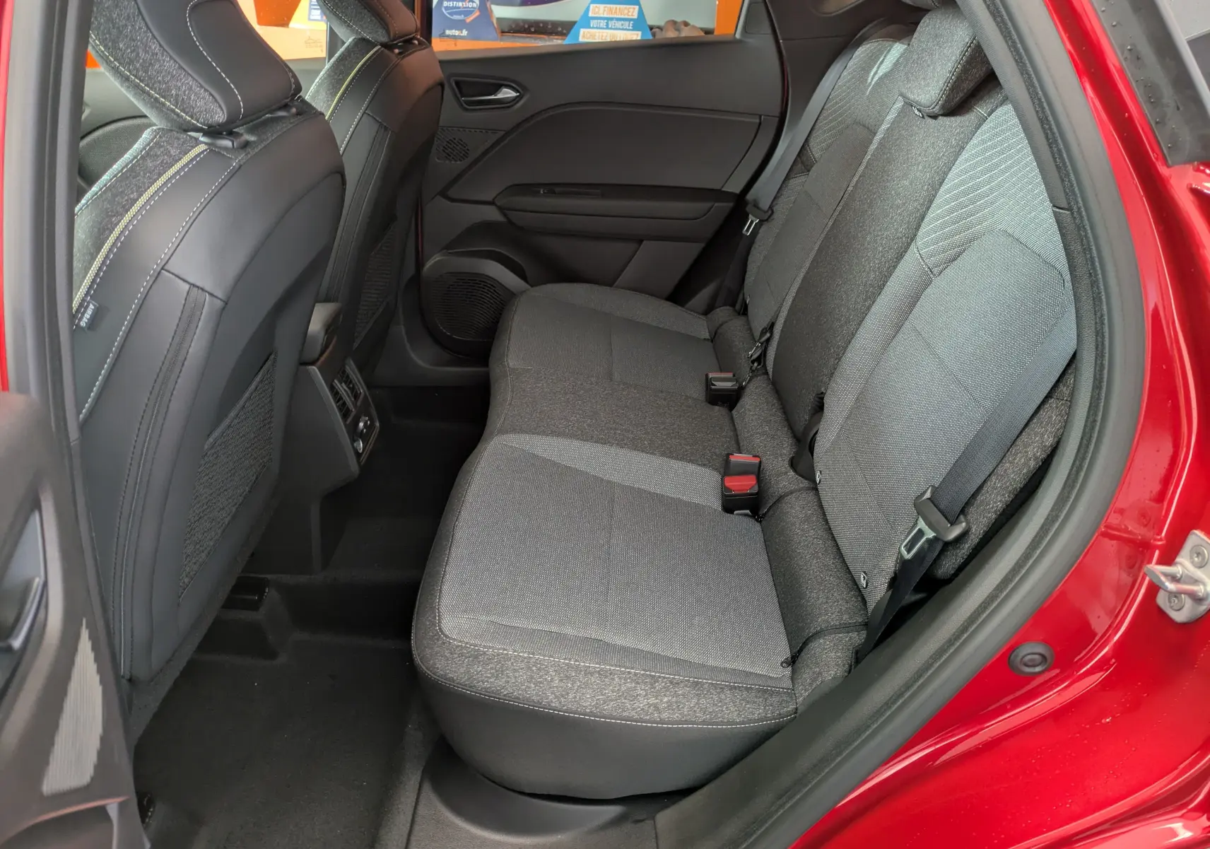Vue intérieure arrière droite du Renault Captur 2025 rouge flamme, montrant les sièges arrière en tissu gris et les portières ouvertes.