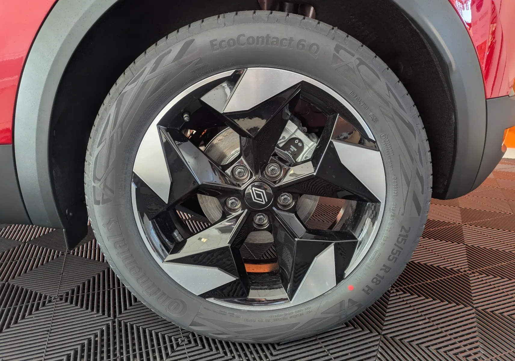 Gros plan sur la roue avant droite du Renault Captur rouge flamme, jante alliage 18'' bicolore noir brillant et argent.
