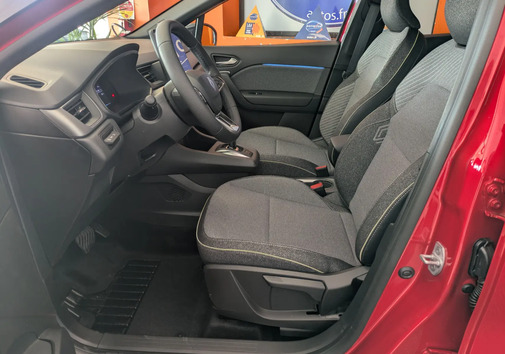 Intérieur côté conducteur du Renault Captur rouge flamme 2025, sièges gris et volant multifonction visible.