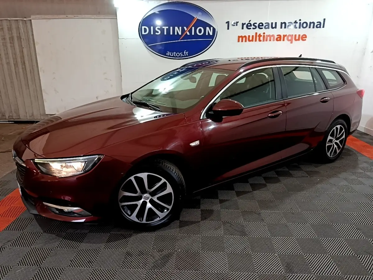 Opel Insignia break rouge vue 3/4 avant droit avec jantes alliage et phares allumés en intérieur showroom.
