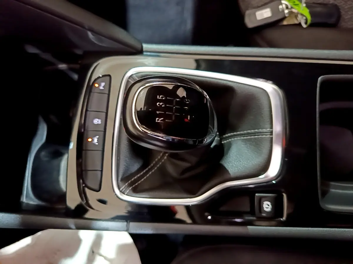 Gros plan sur levier de vitesses manuel noir avec coutures blanches dans console centrale brillante d’Opel Insignia rouge.