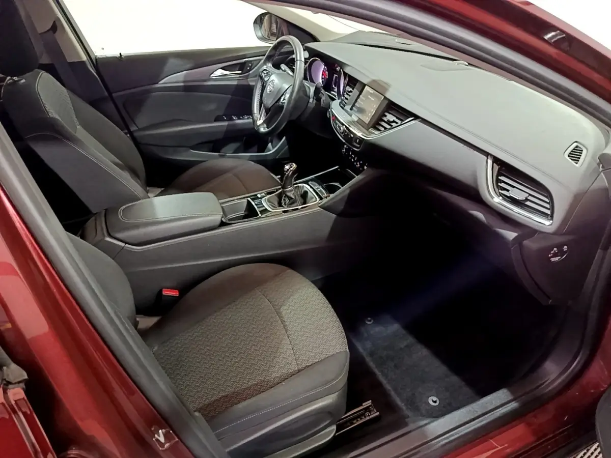 Vue intérieure côté conducteur de l’Opel Insignia rouge, montrant le tableau de bord et la console centrale avec boîte manuelle.