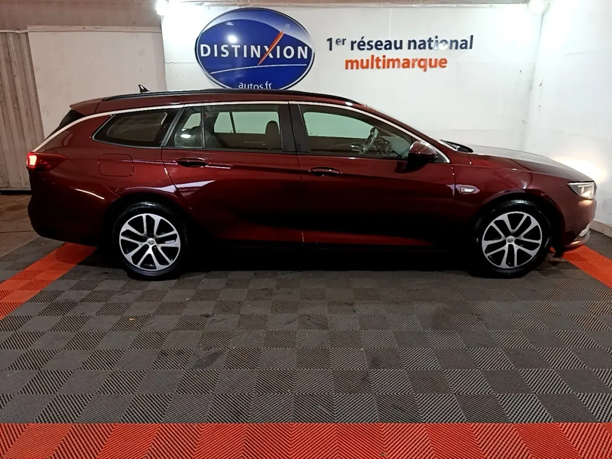 Opel Insignia rouge vue de profil côté gauche, break garé en intérieur avec jantes alliage visibles.
