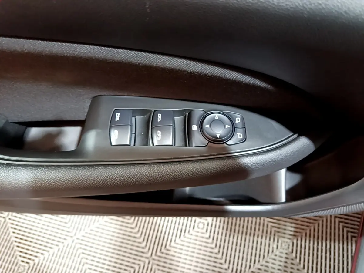 Gros plan sur les commandes des vitres et rétroviseurs côté gauche de la porte intérieure noire d’une Opel Insignia rouge.